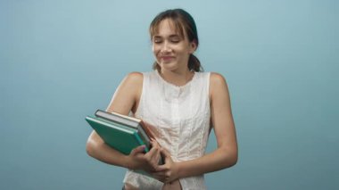 Çıplak kollarıyla yeşil klasöre sarılan ve soluk mavi stüdyoda gülümseyen bir kadın..