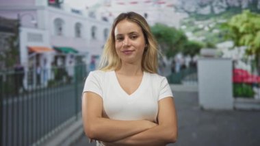 Beyaz tişörtlü kadın parmaklıkların yanında göğsünde baş parmaklarını gösteriyor. Güven onayı iyimserliği..