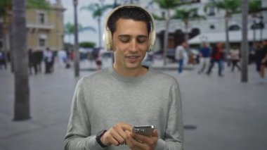 Genç İspanyol adam kulaklıkla müzik dinliyor ve şehirli mahallesinde telefon kullanıyor..