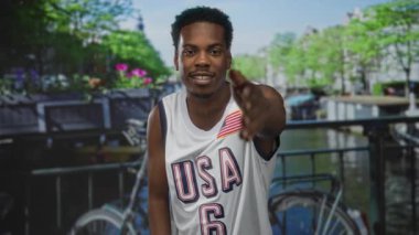 Gülümseyen adam kent caddesinde kanal korkulukları ve park edilmiş bisikletle elini uzatıyor..