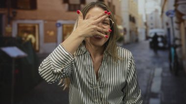 Avrupa 'nın dar kaldırım taşı caddesinde çizgili bluz ve gözlük takan kadın yüzünü gizler;.