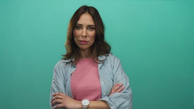 Kollarını kavuşturmuş genç İspanyol kadın yeşil arka plana karşı duruyor. Kendine güvenen ve tarzını belli eden günlük kıyafetler giyiyor..