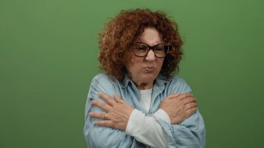 Yeşil arka planda kot ceket giymekten rahatsız olan bir kadın, tenha bir ortamda soğukluk gösteren orta yaşlı bir İspanyol kadını resmediyor..