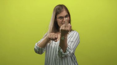 Gözlüklü genç sarışın kadın orta parmağını gösteriyor ve yeşil bir stüdyoda krank çeviriyor..