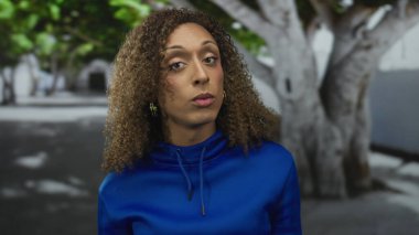 Mavi kapüşonlu kadın açık avuçlu jest ve şehir caddesinde anlamlı yüz gösteriyor..