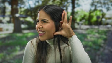 Yeşil bir açık hava parkında dikkatlice dinleyen bir kadın parlak doğal ışık altında tuhaf bir ifade sergiliyor.