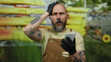 Sakallı, eldiven ve önlüklü bir adam arka planda kanoyla notlar yazar. Odak ve konsantrasyonu canlı manzara ve dinamik ortam arasında yakalar..