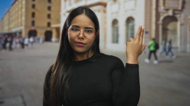 Sokakları işaret eden genç Latin asıllı bir kadın dışarıda sıkılmış bir ifadeye bakıyor..