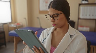 Bir klinik binasında gözlüklü kadın doktor parmak uçlu tablet tıkırdatıyor. Konsantrasyon kendini adamış..