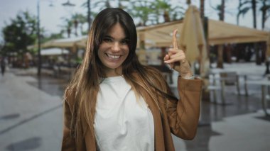 Genç İspanyol kadın gülümsüyor ve canlı bir şehirde arka planda sehpa ve şemsiyelerle bir terasa kuruluyor..