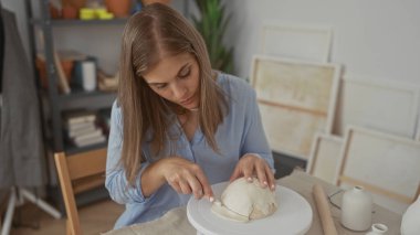 Genç sarışın kadın özenle çömlek kil kubbesini şekillendirir parmakları stüdyoda döner döner döner tablonun üzerinde; yaratıcılık tutkusu dinginliğe odaklanır.