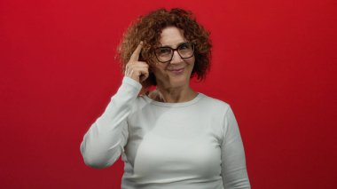 Beyaz gömlekli, parlak kırmızı duvarlı arka planda orta yaşlı, esmer, münzevi Latin kökenli bir kadını işaret ediyor.