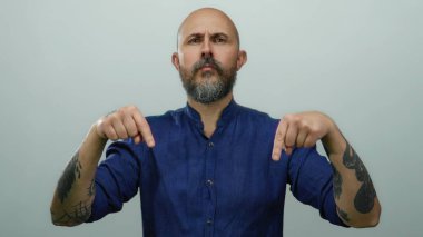 Mavi gömlekli kel adam beyaz arka planda izole edilmiş ciddi bir ifadeyle aşağıya bakıyor.