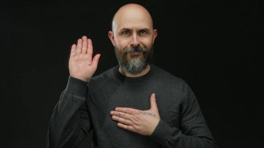 Kel, koyu renk gömlekli bir adam elini göğsüne koyuyor. Siyah bir arkaplana yaslıyor. Samimiyet ve kendine güveni izole stüdyo ortamında resmediyor..