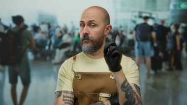 Kel, sakallı ve dövmeli bir adam kalabalığın önünde dikiliyor.