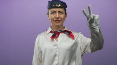Mor stüdyo duvarına karşı beyaz eldivenli, donanma şapkası takan ve kırmızı eşarp takan kadın hostes..