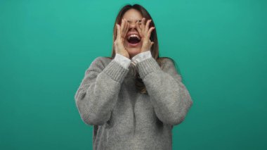 Canlı yeşil bir duvara karşı coşkuyla gülen ve bağıran, rahat bir kazak giyen, neşe ve enerji ifade eden bir kadın..