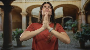 Kadın şehir avlusunda kemerlerle dua ediyor, kırmızı gömlek giyiyor ve minnettarlık ve huzur gösteriyor, şehir ortamında İspanyol kültürünün özünü yakalıyor..