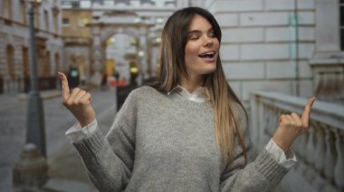 Latin kökenli genç bir kadın, şehir mimarisi arasında pozitiflik ve güven gösteren bir caddeyi neşeyle işaret ediyor..