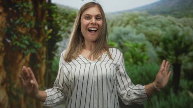 Çıplak omuzlu genç sarışın kadın, parktaki parlak yeşil ağaçların arasında gülümsüyor, hafif esintili, sükunet, huzur ve sükunet..