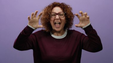 Kıvırcık saçlı ve gözlüklü bir kadın, mor bir fon önünde neşeli, anlamlı ve hayat dolu bir hava yayıyor..