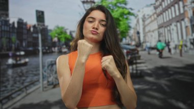 Arkasındaki dar binalar ve kanallı teknelerle günışığı sokağında yumruk kaldıran kadın, kararlılık..