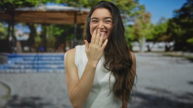 Beyaz kolsuz tişörtlü, ağzı güneşli yeşil park ortamında esneyen İspanyol bir kadın. Sürpriz..