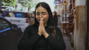 Kalabalık bir sokakta, gözleri kapalı meditasyon yapan bir kadın, sakin bir yüz ifadesi sergiliyor, dinamik bir şehirde dinginliği vurguluyor..