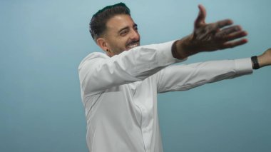 Adam açık avuçlar jesti ile parlak mavi bir stüdyoda kameraya doğru kollarını uzatır; açıklık.