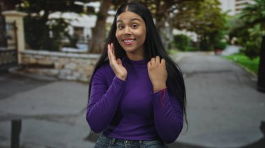 Genç bir kadın, gün ışığında bir şehir sokağında iki eliyle yanaklarına dokunuyor..