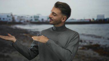 Sıradan, genç İspanyol bir adam, samimi bir gülümseme ve rahat bir duruş ile binanın önünde avuçlarını açık tutuyor..