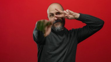 Sakallı adam barışı işaret eder ve enerjik bir şekilde izole edilmiş kırmızı bir arkaplanı işaret eder, anlamlı ve canlı bir portre yaratır..
