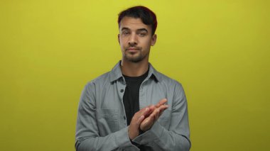 İspanyol adam, izole edilmiş sarı arka planda el çırpıyor. Günlük kıyafetler giyiyor ve anlamlı bir görünüm sergiliyor..