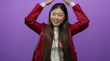 Kırmızı ceketli bir kadın mor bir arka planda neşeli bir şekilde dans ediyor. Kollarını kaldırarak ve dalgalı saçlarıyla mutluluk ve enerji saçıyor..