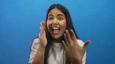 Kadın, Latin kökenli, genç, izole edilmiş mavi arka plan çekimini yaparken elini kaldırıyor..