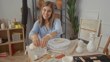 Stüdyoda seramik vazolar ve çanak çömlek aletleri arasında elleri çömlekçi çarkında kil şekillendirir; dinginlik yaratıcılığı.