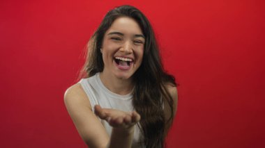 Kadın elini kırmızı bir stüdyoda öpüyor, gözleri kapalı ve dudakları sırıtırken büzüşüyor; şefkat.