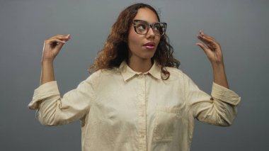 Gözlüklü genç Afrikalı Amerikalı kadın iki elini kaldırdı ve gri stüdyoya baktı..