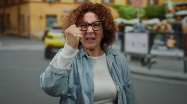 Kentsel sokak ortamında arabalarla hayal kırıklığını ifade eden ve şehir ortamında gözlük takan ve günlük ceket giyen kadınlar..