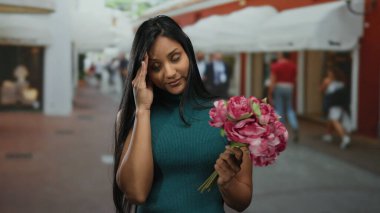 Çiçekleri olan genç bir kadın, arka planda insanlar ve dükkanlarla dolu canlı bir sokakta dalgın dalgın dalgın bakıyor, bir zarafet dokunuşuyla şehir ortamını yakalıyor..
