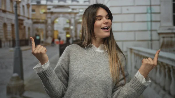 Latin kökenli genç bir kadın, şehir mimarisi arasında pozitiflik ve güven gösteren bir caddeyi neşeyle işaret ediyor..