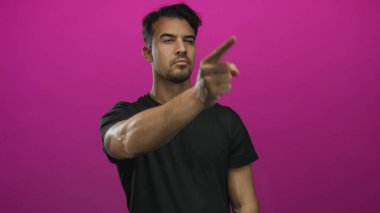 Siyah tişörtlü genç Latin bir adam canlı pembe arka planda parmak göstererek odak ve yönü aktarıyor..