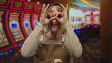 Önlük takan İspanyol kadın kumarhane kumar makinesinde el dürbünü kullanırken gözlere el hareketi yapıyor..