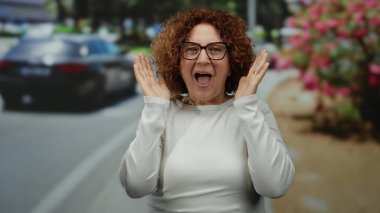 Şehir hayatı ile çevrili bir sokak ortamında, açık havada mutluluğu ve heyecanı ifade eden bir kadın neşeyle tepki veriyor..