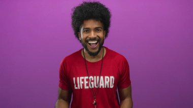 Kırmızı tişört giyen kıvırcık saçlı cankurtaran, izole edilmiş pembe arka plana, neşeli duygulara ve enerjik gençlik enerjisine karşı mutluluğu ifade ediyor..