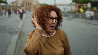Kalabalık bir şehir caddesinde dikkatle dinleyen kadın, çeşitli arka plan unsurlarına sahip bir şehir ortamında merak ve bağlılık sergiliyor..