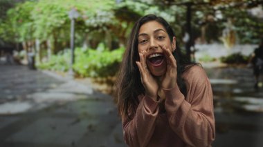 Yeşil park yolunun yakınındaki sokakta el ele tutuşup bağıran, kahverengi kazak giyen, bol bol gülümseyen, neşe dolu bir kadın..