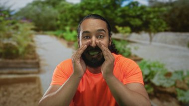 Ağızdan ağıza avuçlayan adam orman yolunda yeşil yapraklı turuncu tişört giyerek sesleniyor. Uyarı uyarısı..