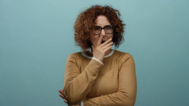Gözlüklü bir kadın sakin bir günde mavi bir arka planda esniyor. Kıvırcık saçlı ve düşünceli bir tavır takınıyor..