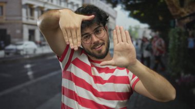 Sakallı, kırmızı çizgili tişörtlü, şehir caddesinde elleri olan, neşeli bir şekilde gülümseyen, güneşli bir gün.